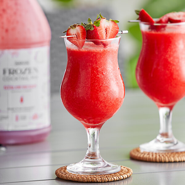 A bottle of Narvon Strawberry Frozen Cocktail Mix with two glasses of red strawberry drink.