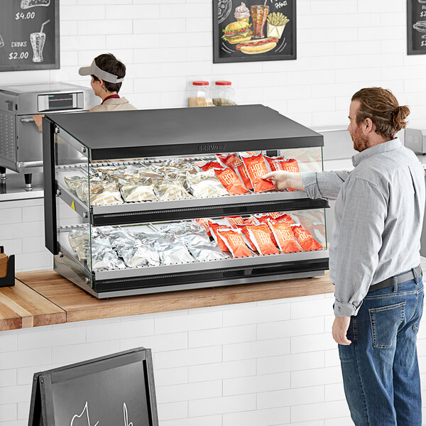 A man looking at a ServIt countertop heated display case filled with food.