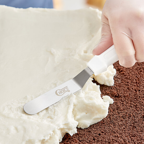 A person using a Choice white offset baking / icing spatula to frost a cake.
