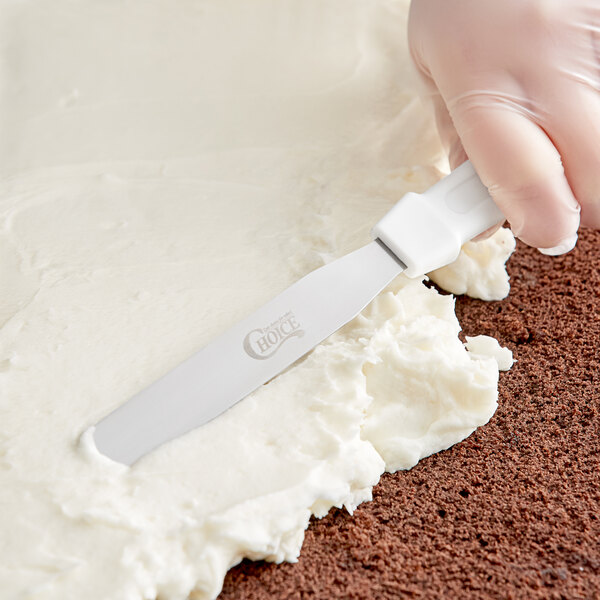 A gloved hand uses a Choice straight baking / icing spatula with a white plastic handle to cut a cake.