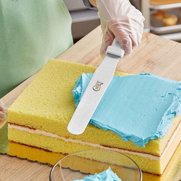 A person using a Choice straight baking spatula with a yellow sponge cake.