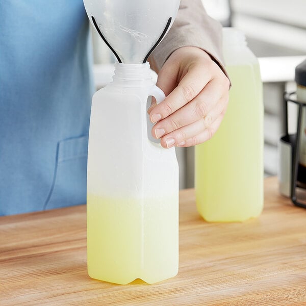 A hand pouring liquid into a white translucent HDPE jug with a handle.