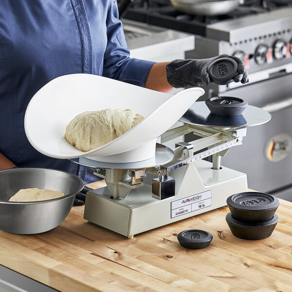 A person weighing dough on an AvaWeigh baker's dough scale with a black bowl.
