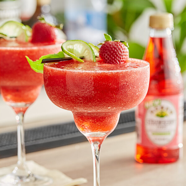 Two glasses of strawberry margaritas garnished with a strawberry on a table.