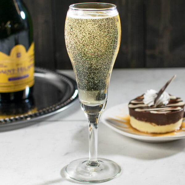 A close up of a Libbey tulip champagne glass filled with champagne next to a plate of dessert.