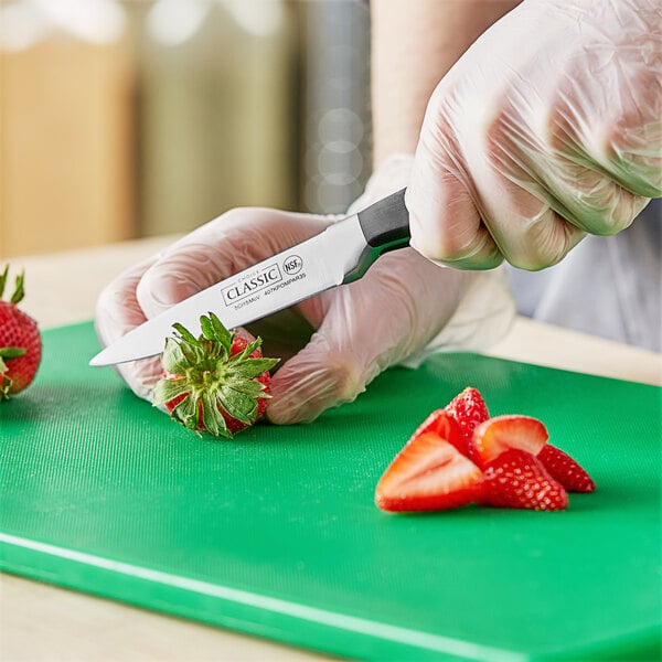 A person using a Choice Classic paring knife to cut strawberries on a cutting board.