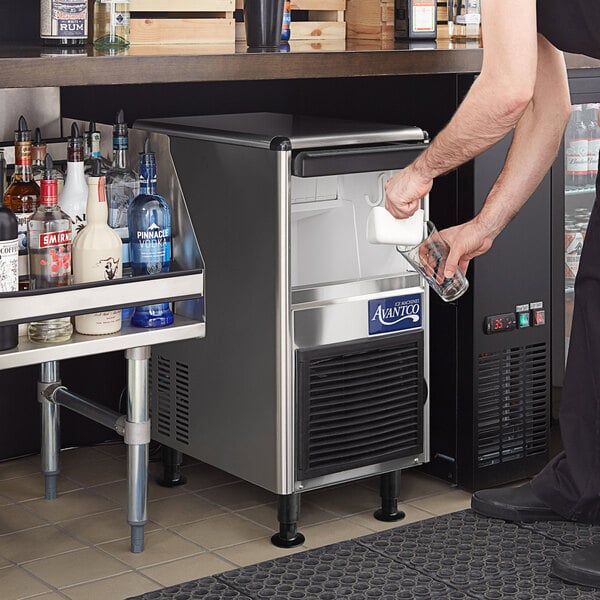 An Avantco undercounter ice machine on a bar counter with a man pouring a drink.