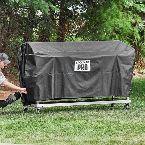 A person pushing a black Backyard Pro vinyl cover over a barbecue.
