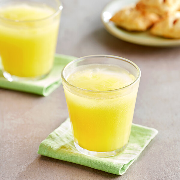 A glass of yellow pineapple juice on a green napkin next to a plate of pastries.