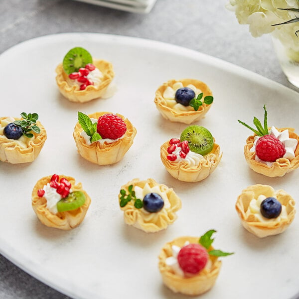 A plate of Fillo Factory mini pastry baskets filled with fruit, one topped with a blueberry.