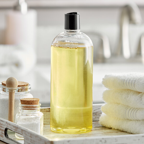 A Boston round clear plastic bottle with black disc top lid containing yellow liquid sits on a tray with towels.