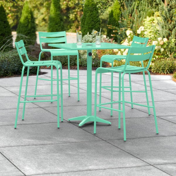 A Lancaster Table & Seating seafoam green table with 4 barstools on a patio.