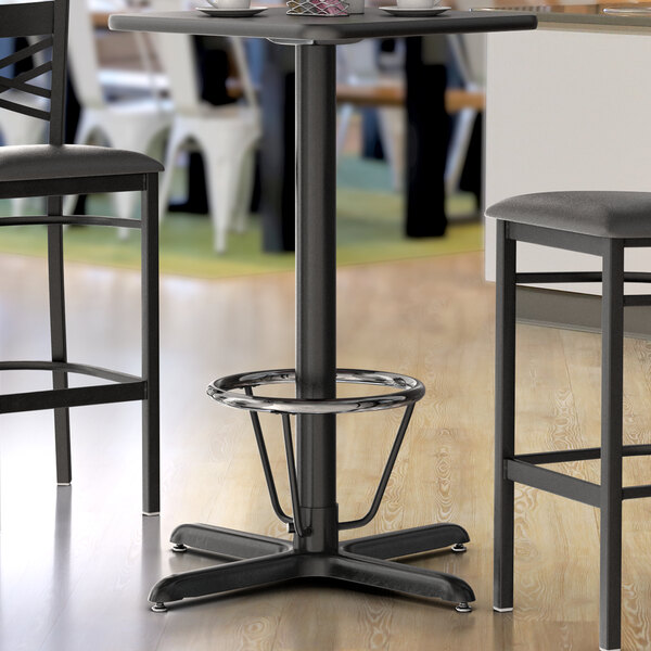 A close-up of a black Lancaster Table & Seating bar height table base with a metal foot ring.