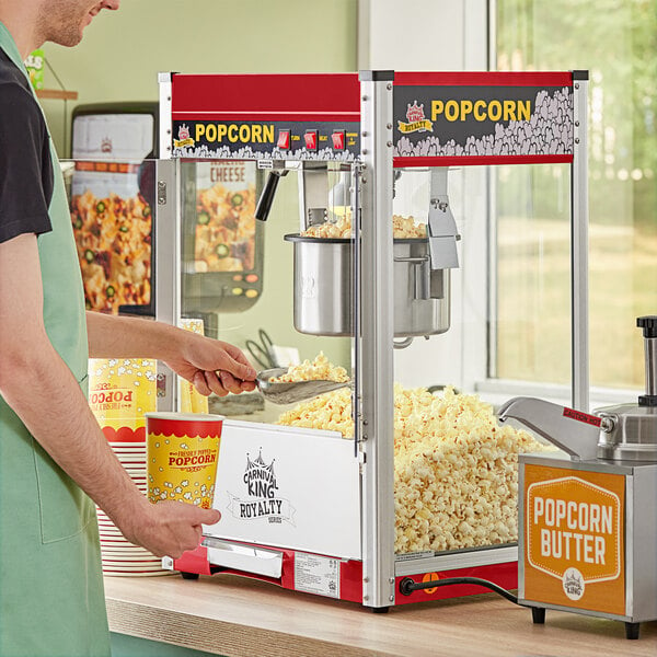 A man in a green apron prepares popcorn in a red Carnival King popcorn machine.