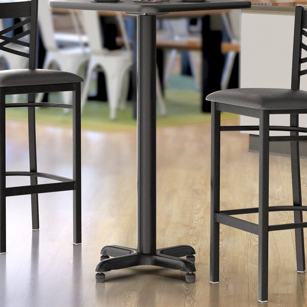 A black Lancaster Table & Seating bar table base with two chairs.