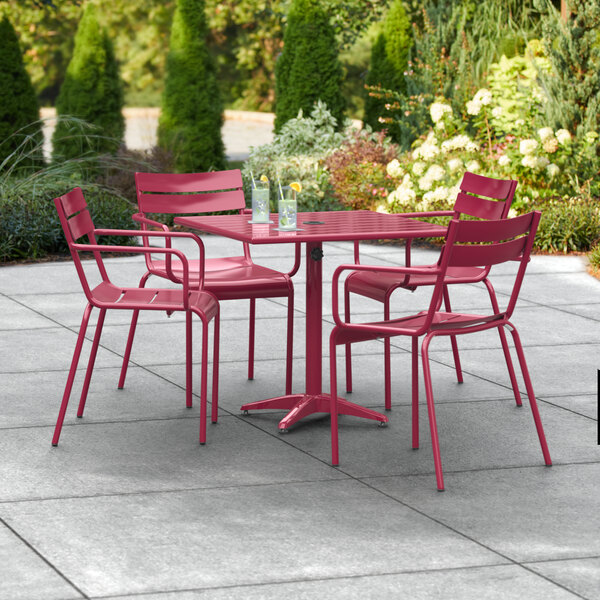 A Lancaster Table & Seating outdoor table with red chairs and an umbrella on a patio.