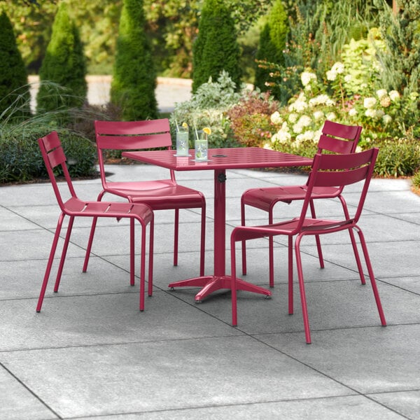 A Lancaster Table & Seating outdoor patio table with red chairs and an umbrella hole.