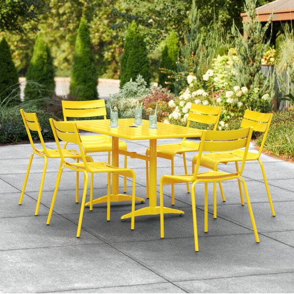A yellow table with an umbrella hole and six yellow chairs on a patio.