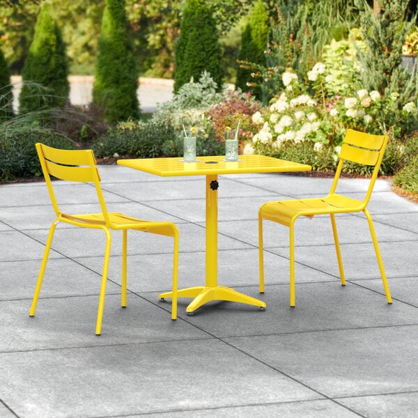 A yellow table and two chairs on a stone patio.