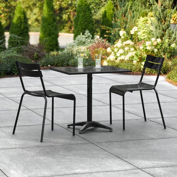 A black Lancaster Table & Seating outdoor table and two chairs on a patio.