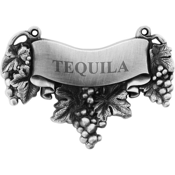 A silver metal Franmara decanter label with a grape vine and leaves above the word "Tequila"