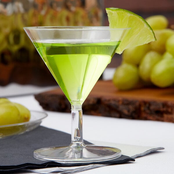 A clear Fineline Tiny Tinis plastic glass filled with green liquid and a lime wedge on the rim.