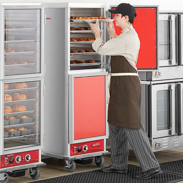 A man in a brown apron standing next to an Avantco heated holding cabinet with solid Dutch doors.