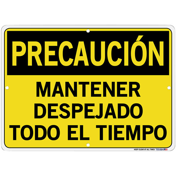 A white aluminum warehouse sign with yellow and black text reading "Precauci&#243;n / Mantener Despejado Todo El Tiempo"