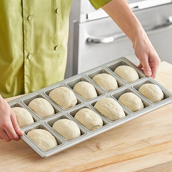 A hand holding a Baker's Mark 12 compartment mini bread pan filled with dough balls.