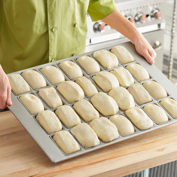 A person holding a tray of dough with Baker's Mark aluminized steel mini bread pans.