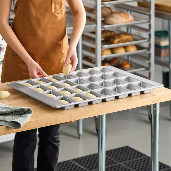 A 28-compartment glazed aluminized steel mini bread pan with rectangular cavities, used for baking small loaves of bread.