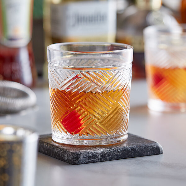 An Acopa Zion old fashioned glass with a drink on a stone coaster.