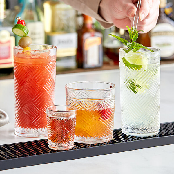 A bartender pours drinks into Acopa Zion old fashioned glasses on a bar.