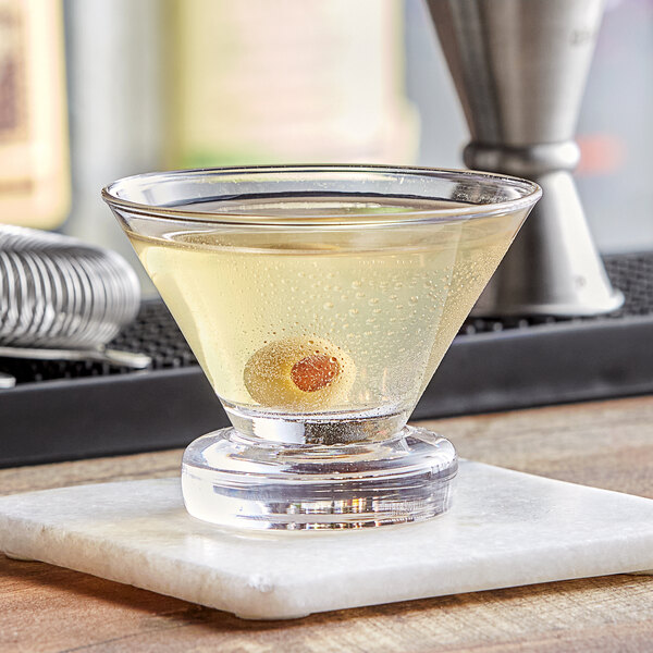 A Fortessa Temptationz martini glass filled with a cocktail and garnished with olives on a table in a cocktail bar.