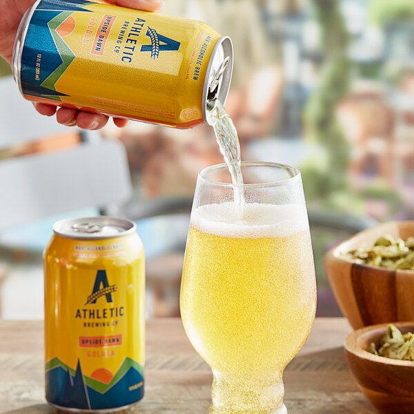 A hand pouring Athletic Brewing Co. Upside Dawn non-alcoholic golden beer from a yellow can into a glass.