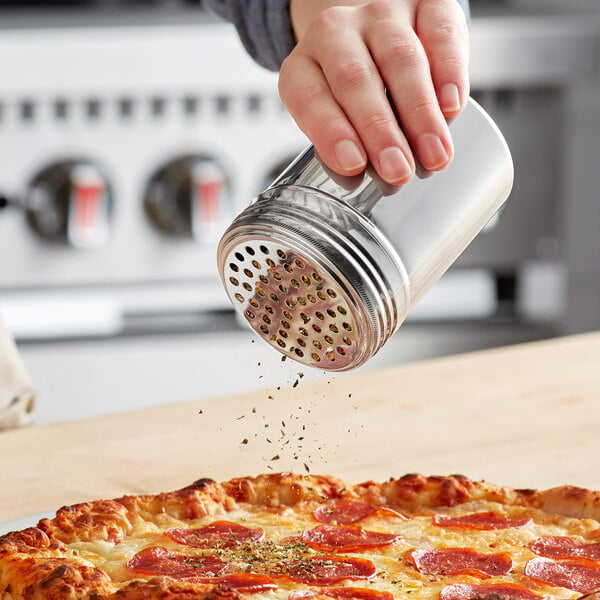 A hand using a Choice stainless steel shaker to add pepper seasoning to a pizza.