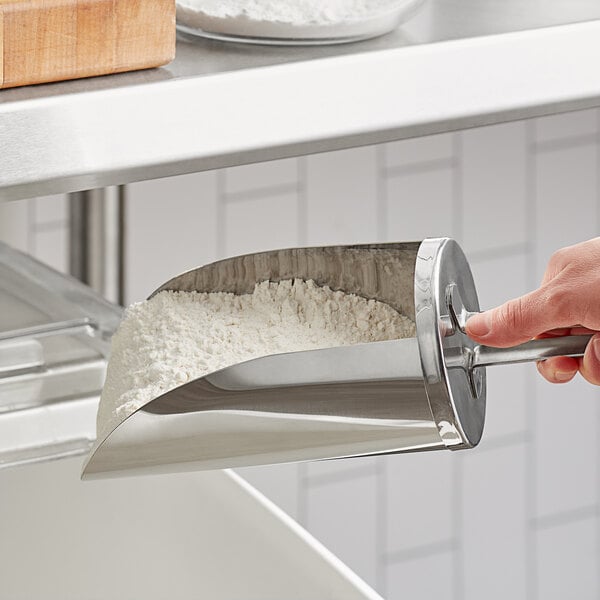 A hand using a Choice stainless steel flour scoop to scoop flour.