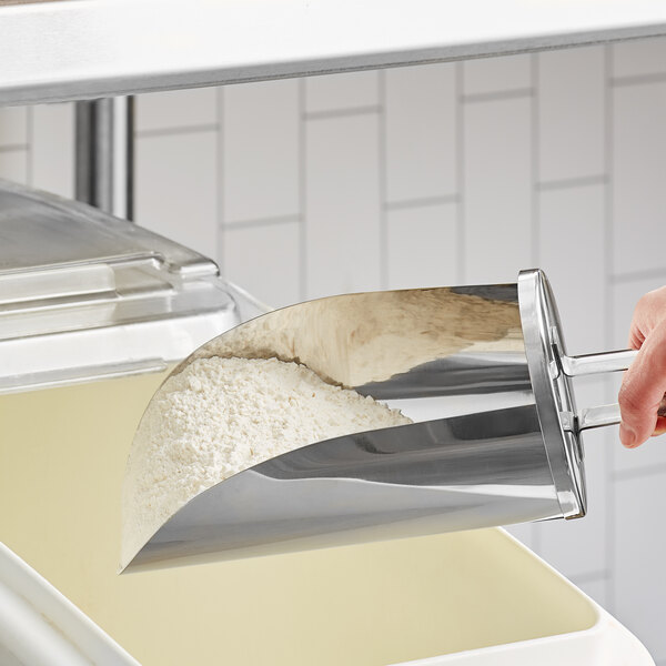 A hand using a Choice stainless steel flour scoop to put flour in a container.