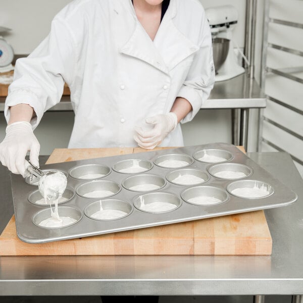 A woman in a white coat using a Chicago Metallic mini cake and muffin pan to pour batter.