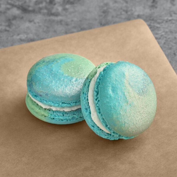 Two blue and green Macaron Centrale Earth macarons on a brown surface.