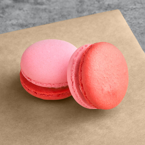 Two pink and red Macaron Centrale macarons on a brown surface.
