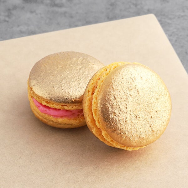 Two gold raspberry macarons on a table.
