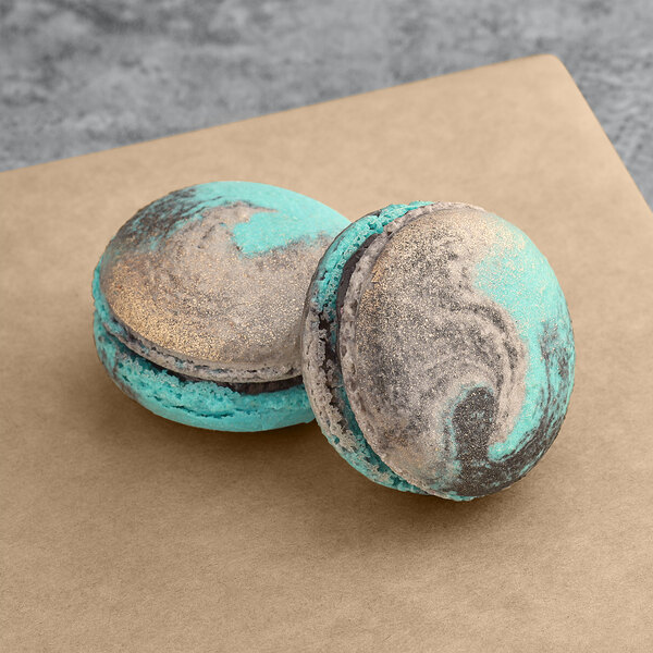 Two blue and silver Macaron Centrale Mercury macarons on a brown surface.