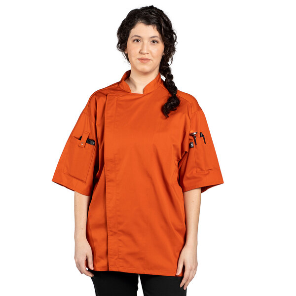 An woman wearing an orange Uncommon Chef Venture Pro Vent short sleeve chef coat with black buttons.