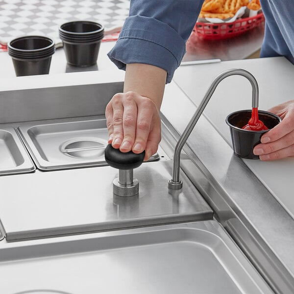 A person using a ServSense stainless steel pump to pour red liquid into a black cup.