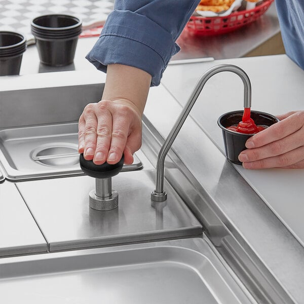 A person using a ServSense stainless steel pump to pour ketchup into a black cup.