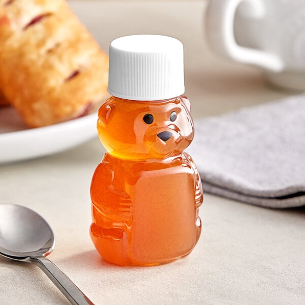 A clear plastic bear-shaped honey bottle with a white lid on a table with a spoon.