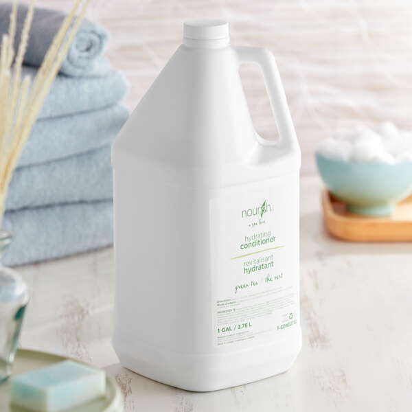 A white jug of Nourish Green Tea conditioner with a green label on a table next to towels.