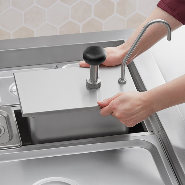 A person using a ServSense stainless steel pump dispenser on a counter.