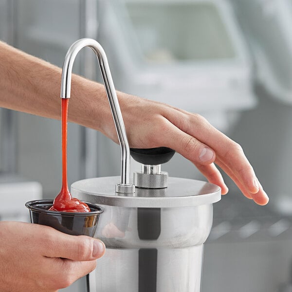 A hand using a ServSense stainless steel pump to pour ketchup into a cup.